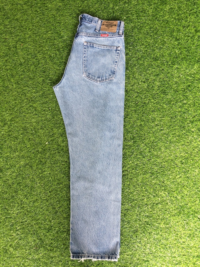 May include: A pair of light blue denim jeans with a brown leather patch on the back waistband that says "Wrangler" and "Premium Western Denim".