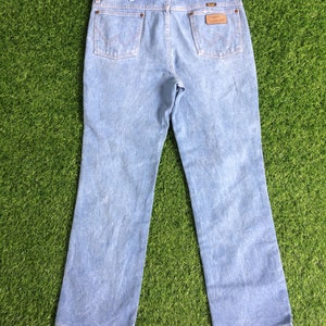May include: A pair of light blue denim jeans with a brown leather patch on the back pocket that says "Wrangler".