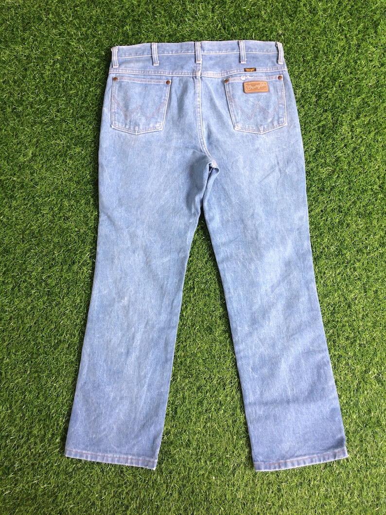 May include: A pair of light blue denim jeans with a brown leather patch on the back pocket that says "Wrangler".