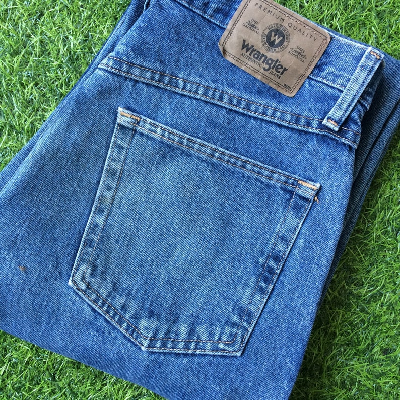 May include: A pair of blue denim jeans with a back pocket and a brown leather patch that says "Wrangler Authentic Brand" with a white "W" logo.