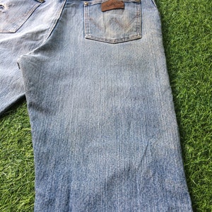 May include: A pair of light blue denim jeans with a brown leather patch on the back pocket that says "Wrangler".