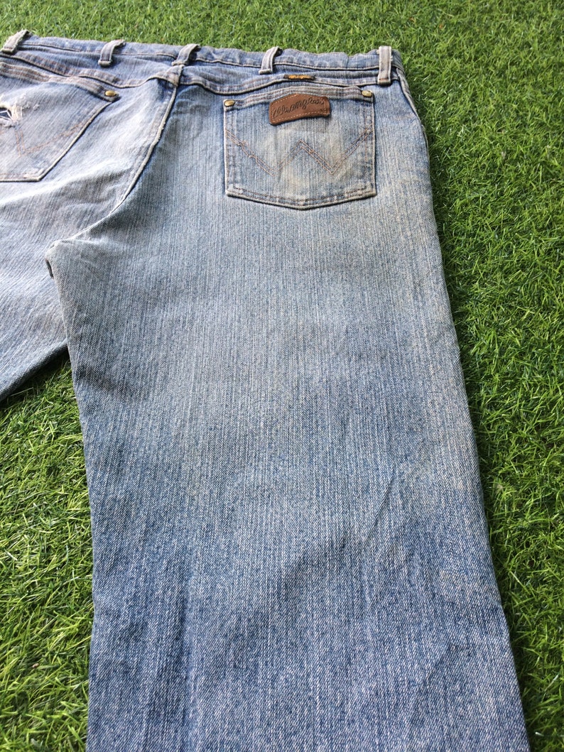 May include: A pair of light blue denim jeans with a brown leather patch on the back pocket that says "Wrangler".