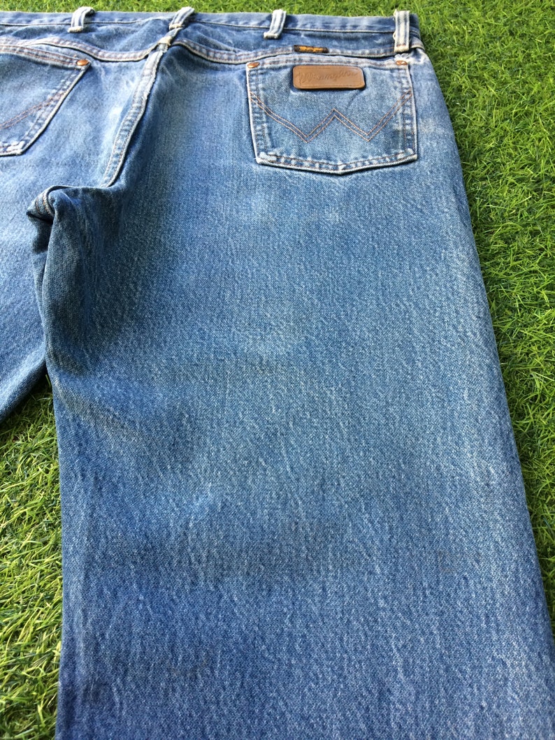 May include: A pair of blue denim jeans with a brown leather patch on the back pocket that says "Wrangler".