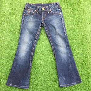 May include: Blue denim jeans with a flared leg design. The jeans feature a classic five-pocket style, with decorative stitching and a button closure. The denim has a faded wash effect, and the stitching is in a contrasting orange color.