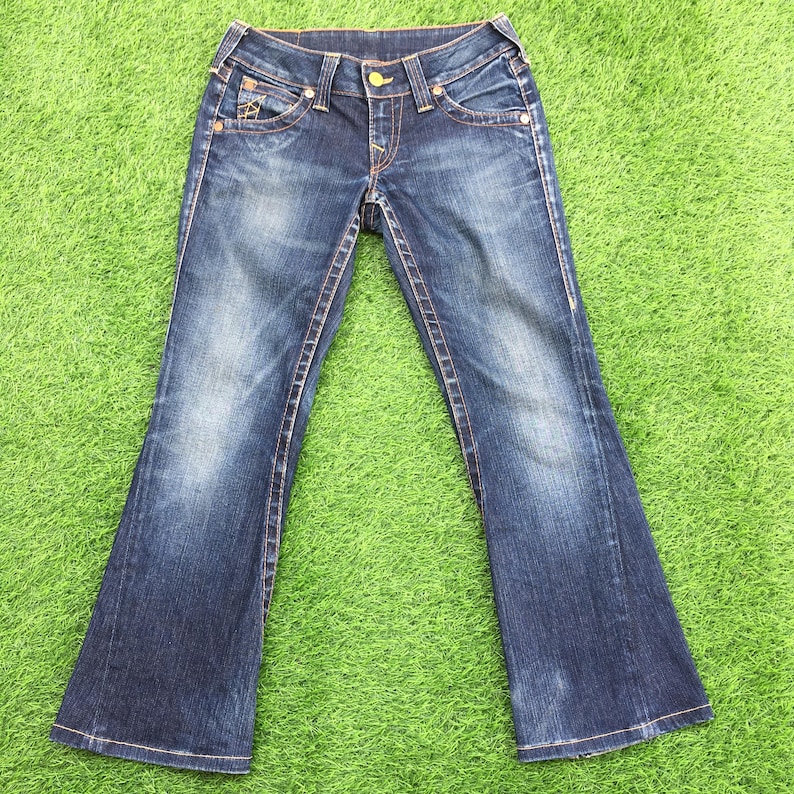 May include: Blue denim jeans with a flared leg design. The jeans feature a classic five-pocket style, with decorative stitching and a button closure. The denim has a faded wash effect, and the stitching is in a contrasting orange color.