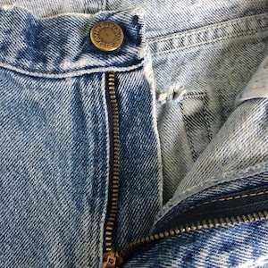 May include: Close-up of a blue denim zipper with a brass zipper pull that says "YKK". The zipper is partially open and the denim is faded.