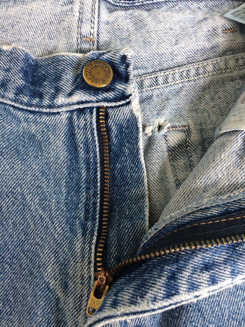 May include: Close-up of a blue denim zipper with a brass zipper pull that says "YKK". The zipper is partially open and the denim is faded.