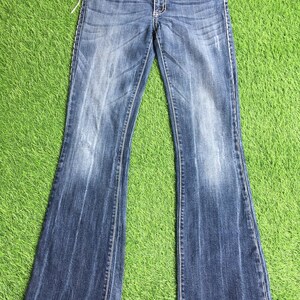 Op de afbeelding: Een paar blauwe denim jeans met een bootcut-poot. De jeans heeft een lichte wassing en is distressed met fading en whiskering. De jeans heeft een gouden knoop en ritssluiting en een klein geborduurd logo op de achterzak.