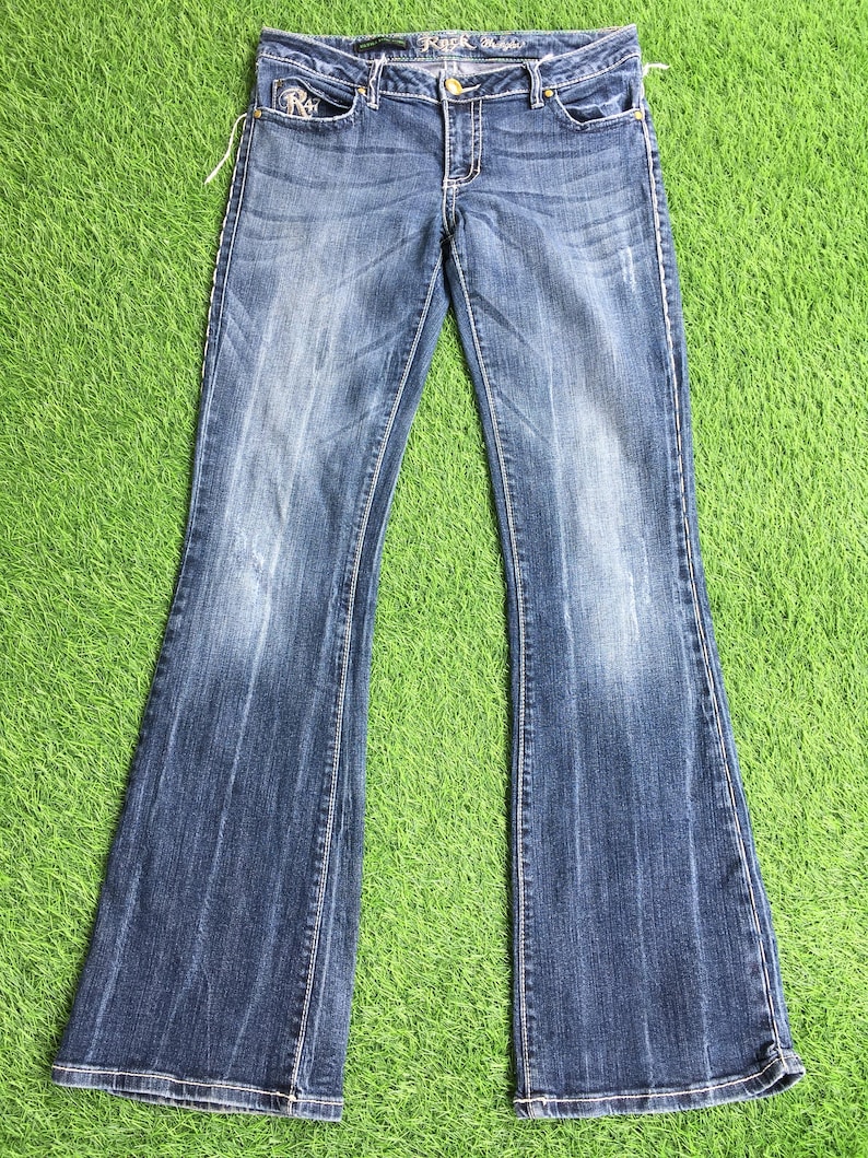 Op de afbeelding: Een paar blauwe denim jeans met een bootcut-poot. De jeans heeft een lichte wassing en is distressed met fading en whiskering. De jeans heeft een gouden knoop en ritssluiting en een klein geborduurd logo op de achterzak.
