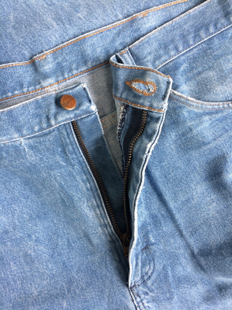 May include: Close-up of a pair of blue denim jeans with a zipper and a button closure. The zipper is partially open.