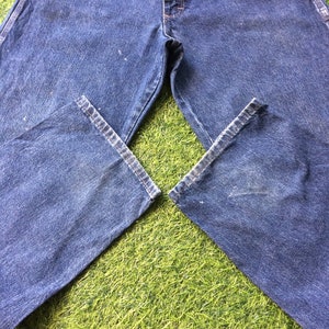 May include: A pair of blue denim carpenter jeans laid out on a green grassy surface.