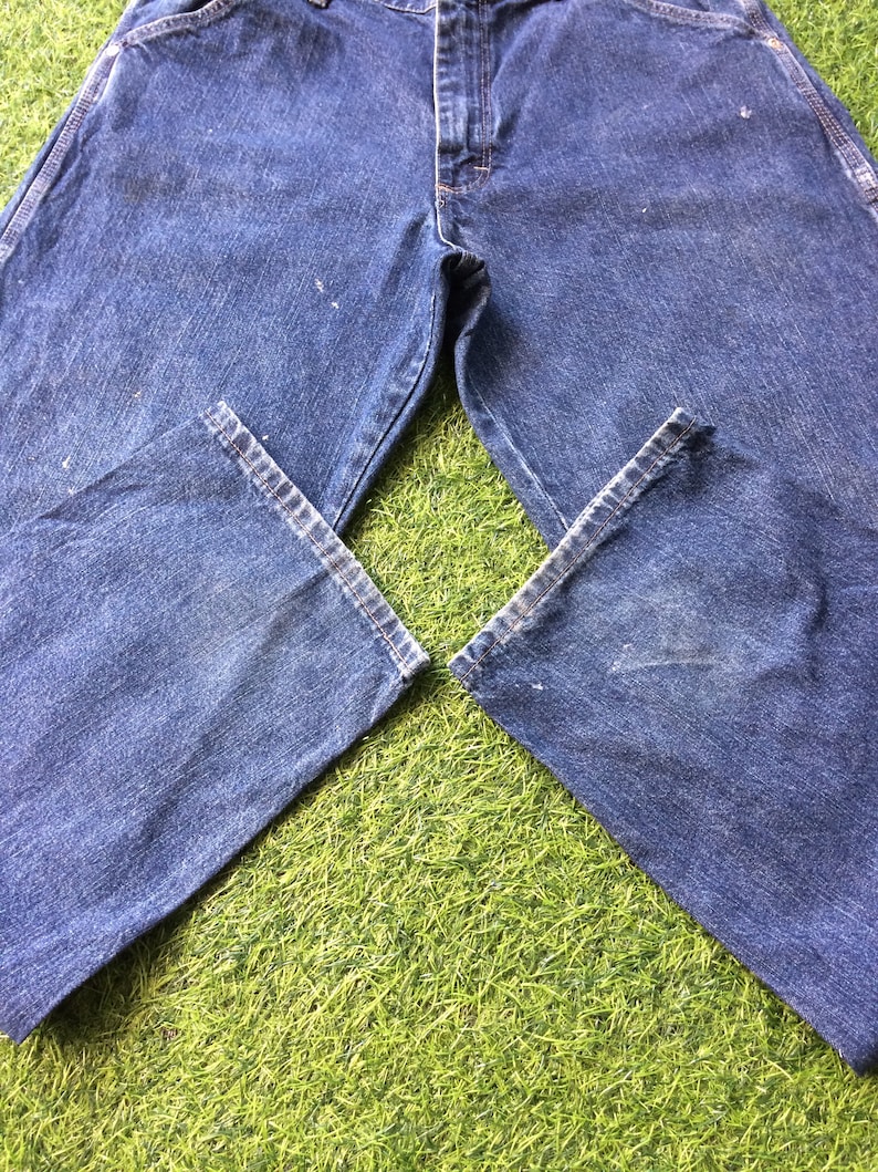 May include: A pair of blue denim carpenter jeans laid out on a green grassy surface.