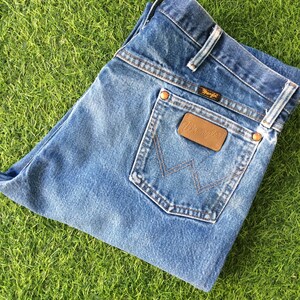 May include: A pair of blue denim jeans with a brown leather Wrangler patch on the back pocket.