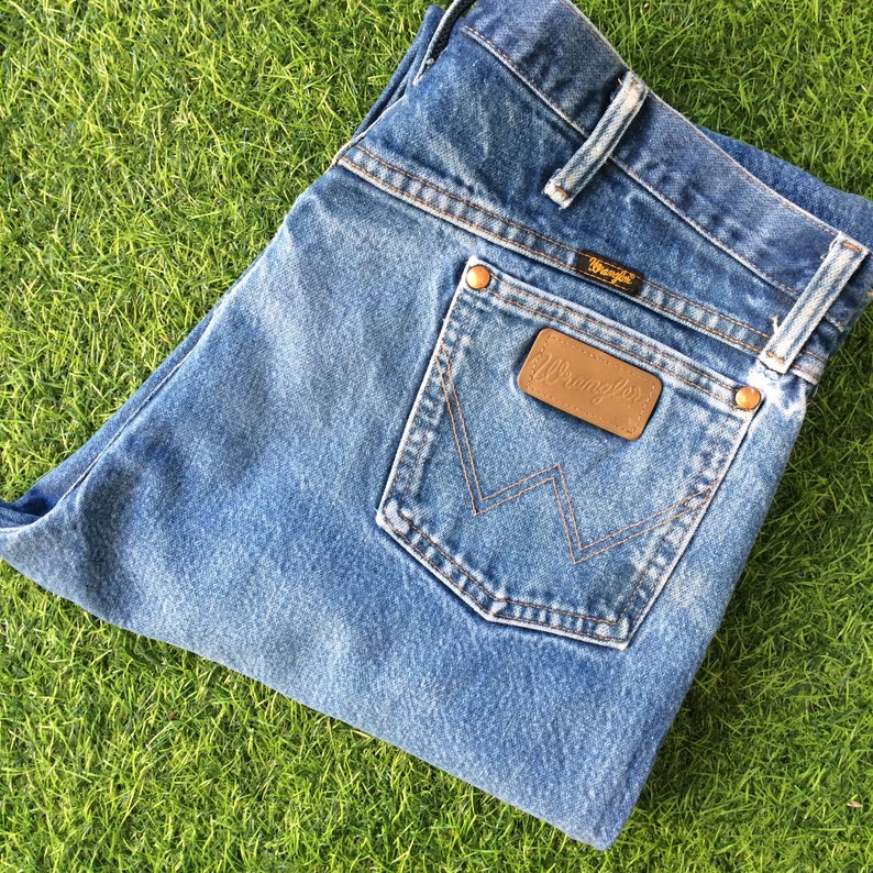 May include: A pair of blue denim jeans with a brown leather Wrangler patch on the back pocket.