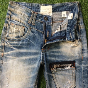 May include: Distressed blue denim jeans with a zippered pocket and the word "Lolita" on the zipper pull. The jeans have a size tag that says "S".