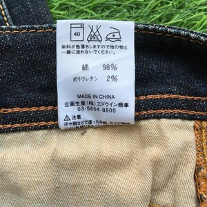 May include: Close-up of a denim jeans label with Japanese text and care symbols. The label indicates the fabric composition: 98% cotton and 2% polyurethane. The label also includes the text "MADE IN CHINA".
