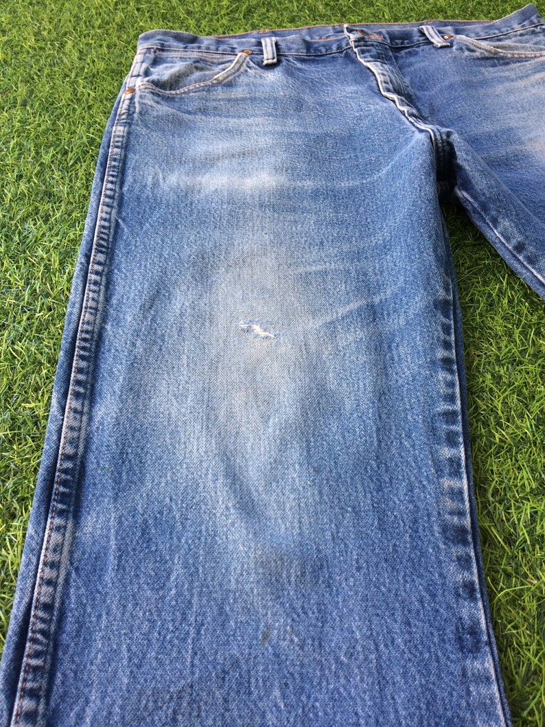 May include: A pair of blue denim jeans with a faded look and a small hole on the left leg.