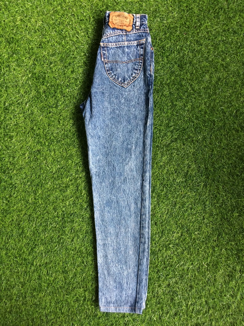 May include: Light blue acid wash denim jeans with a brown leather patch that says "Something Special" on the back.