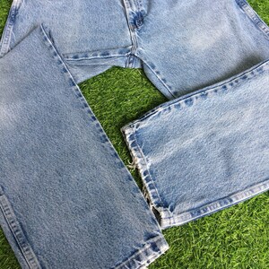 May include: A pair of light blue denim jeans with a faded wash and frayed hems. The jeans are laid out on a green grassy surface.