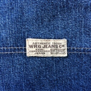May include: A close-up of a blue denim fabric with a white label that reads "Authentic Issue WRG Jeans Co. Real Comfortable Jeans Est. 1947".
