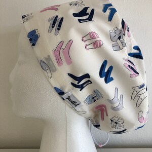 May include: White scrub hat with a blue and pink shoe print pattern. The hat has a drawstring and the text "Scruffed" is printed on the side.