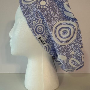May include: A purple scrub hat with a white and purple patterned design. The hat has a tie on the back and the word "Scrubbed" is printed on the side.
