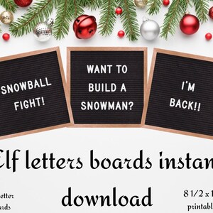 May include: Three black letter boards with wooden frames, each displaying a different Christmas-themed message: "SNOWBALL FIGHT!", "WANT TO BUILD A SNOWMAN?", and "I'M BACK!!". The boards are surrounded by Christmas decorations, including red and silver ornaments and a green pine branch.