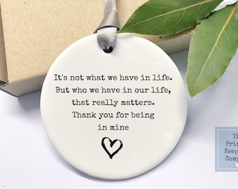 May include: White ceramic ornament with black text that reads "It's not what we have in life. But who we have in our life, that really matters. Thank you for being in mine." A small black heart is drawn at the bottom of the text.
