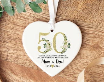 May include: White heart-shaped ceramic ornament with gold glitter 50 and floral design. The ornament reads "Congratulations on your Golden Wedding Anniversary Mum & Dad 1974 ♥ 2024".