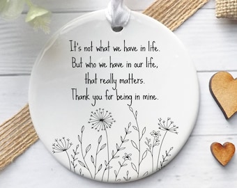 May include: White ceramic ornament with black text and a floral design. The text reads "It's not what we have in life. But who we have in our life, that really matters. Thank you for being in mine."