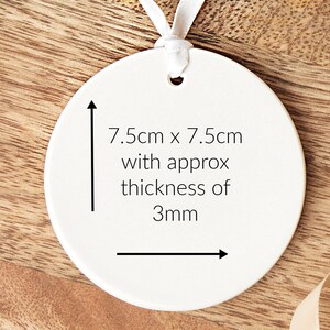 Pode incluir: Ornamento redondo de cer&acirc;mica branca com uma fita branca presa. O ornamento mede 7,5 cm por 7,5 cm e tem uma espessura aproximada de 3 mm.
