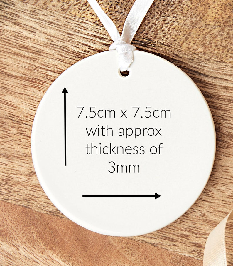 Pode incluir: Ornamento redondo de cer&acirc;mica branca com uma fita branca presa. O ornamento mede 7,5 cm por 7,5 cm e tem uma espessura aproximada de 3 mm.