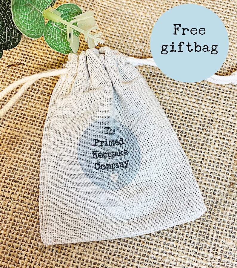 Pode incluir: Uma pequena bolsa de cord&atilde;o de cor branco-creme, feita de tecido natural. A bolsa tem um logotipo circular preto com o texto "The Printed Keepsake Company". A bolsa est&aacute; sobre uma superf&iacute;cie de juta marrom. Um c&iacute;rculo azul com o texto "Free giftbag" est&aacute; no canto superior direito da imagem.