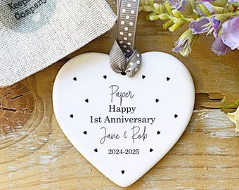 May include: White ceramic heart ornament with black text that reads "Paper Happy 1st Anniversary Jane & Rob 2024-2025". The ornament is decorated with small black hearts.