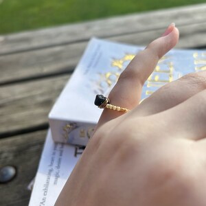 May include: A gold wire ring with a black gemstone. The ring is on a finger.