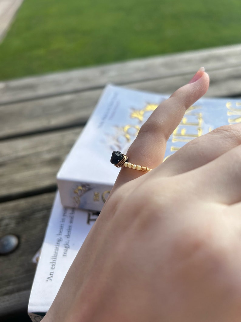 May include: A gold wire ring with a black gemstone. The ring is on a finger.