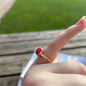 May include: A gold wire ring with a red gemstone and white beads.