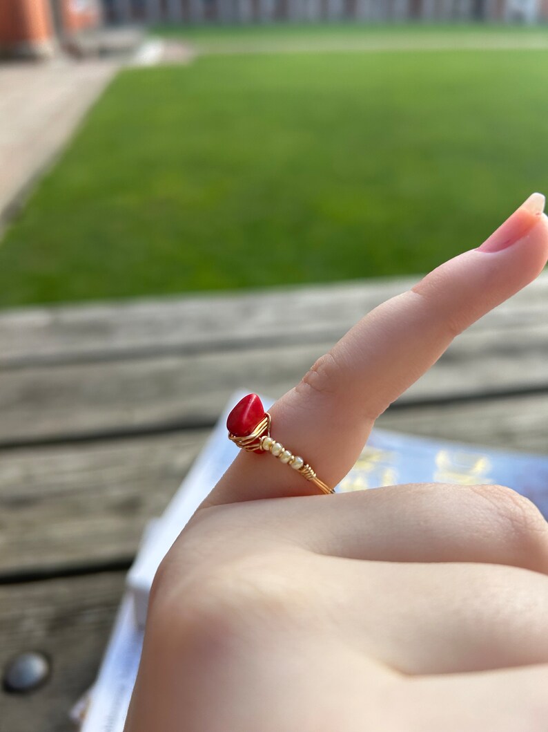 May include: A gold wire ring with a red gemstone and white beads.