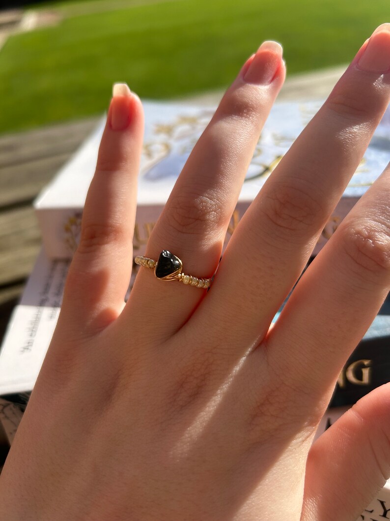 May include: A gold ring with a black heart-shaped stone. The ring is on a finger.