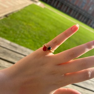May include: A gold ring with a red and black heart-shaped stone. The ring is on a person's finger.