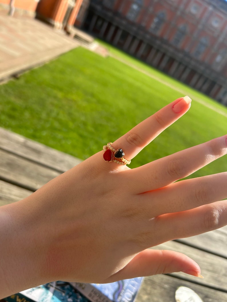 May include: A gold ring with a red and black heart-shaped stone. The ring is on a person's finger.