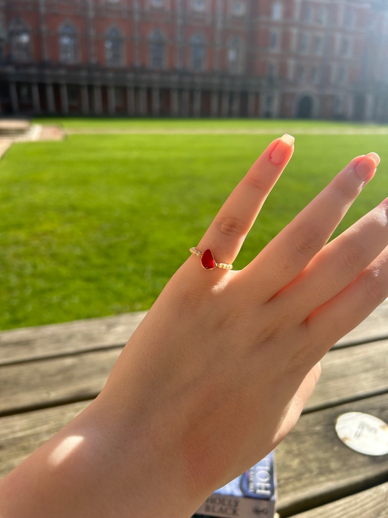 May include: A gold ring with a red teardrop-shaped stone and small white beads around the band.