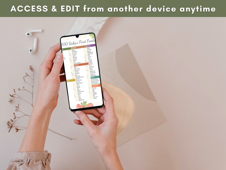 May include: A person is holding a smartphone displaying a digital checklist titled "100 Baby's First Foods". The checklist is organized into categories, including fruits, vegetables, grains, and proteins. The phone is on a light brown surface.