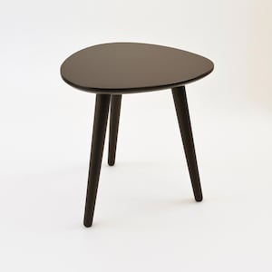 May include: A black, three-legged side table with a rounded, oval-shaped top.
