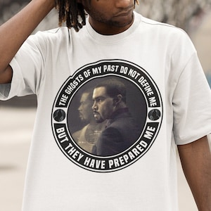 May include: White t-shirt with a black and white circular graphic featuring a man's face and the text "The Ghosts of My Past Do Not Define Me But They Have Prepared Me."