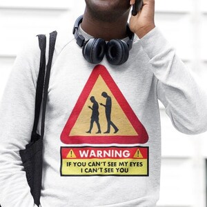 May include: A gray sweatshirt with a warning sign graphic. The sign is red and yellow with a black silhouette of two people walking. The text on the sign reads "Warning! If you can't see my eyes I can't see you."