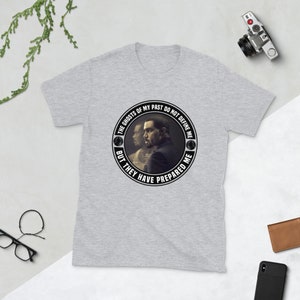 May include: Gray t-shirt with a black and white circular graphic featuring a man's face and the text "THE GHOSTS OF MY PAST DO NOT DEFINE ME BUT THEY HAVE PREPARED ME".