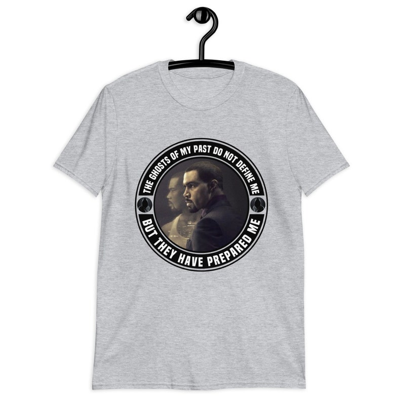May include: A grey t-shirt with a black and white circular graphic featuring a man's face and the text "THE GHOSTS OF MY PAST DO NOT DEFINE ME BUT THEY HAVE PREPARED ME".