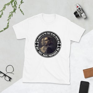 May include: White t-shirt with a black and white circular graphic featuring a man's face and the text "The ghosts of my past do not define me but they have prepared me."
