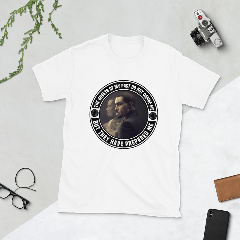 May include: White t-shirt with a black and white circular graphic featuring a man's face and the text "The ghosts of my past do not define me but they have prepared me."